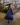 Woman in blue raincoat and holding an umbrella walking on a sidewalk.